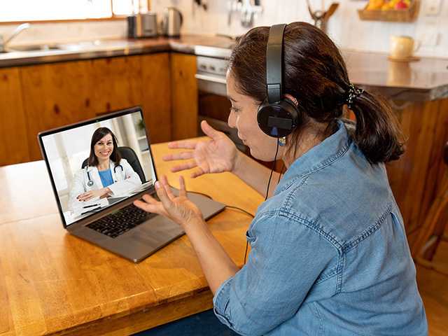 woman sitting at dinner table speaking to a doctor on her laptop computer