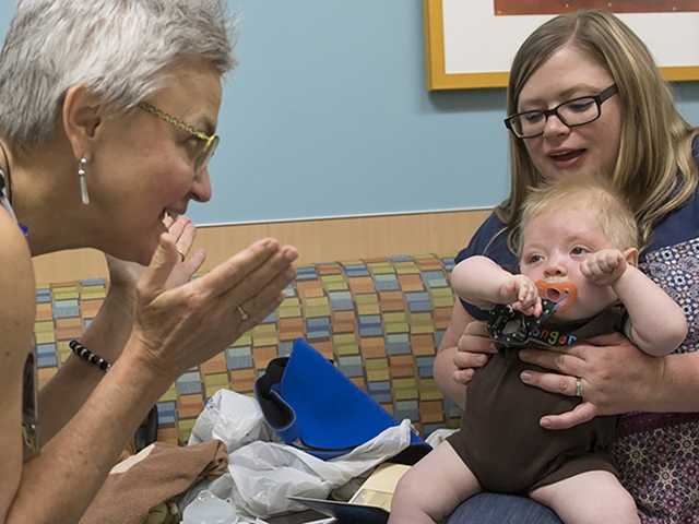 Healthcare Provider talks to baby sitting on mothers lap.