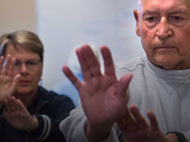 Older man in gray shirt with hand stretched out in front of him with concentration on his face