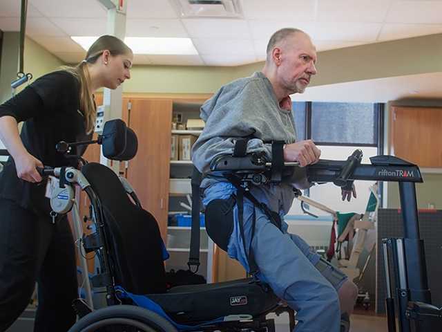 Man getting assistance to get out of wheelchair from two female physical therapists.